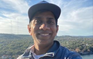 A man smiling, with a backdrop of trees and a horizon