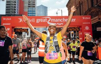A woman celebrating at the finish line of a sponsored running event, with her hand in the air