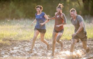 Two women and a man running through mud