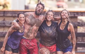 Three women and a man covered in mud posing together at the end of race