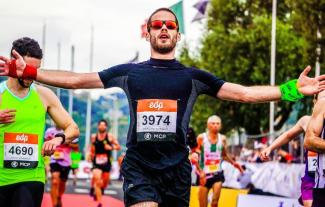 A man in sunglasses crossing the finish line at a sponsored run, with arms outstretched