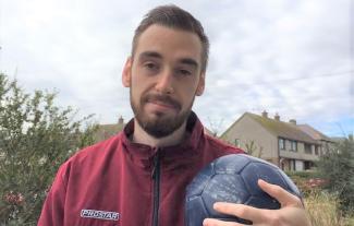 A man in a tracksuit holding a football and smiling