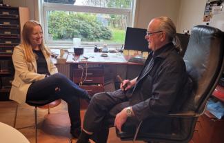 A woman and a man seated in an office, facing each and talking