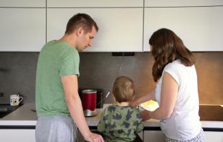A mother and father cooking at a stove, with a young child between them, facing the stove