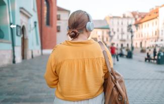 The back of a woman wearing headphones as she faces a street scene.