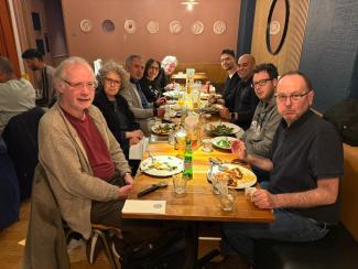 Nine people, six men and three wome, sitting at a restaurant table and smiling