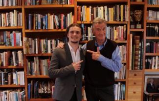 Sir Michael Palin posing with a man and both are smiling at pointing at each other