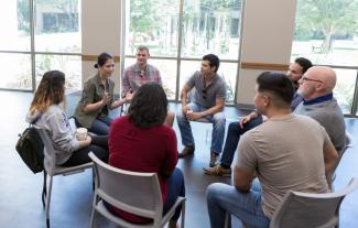 People sitting in chairs in a circle, in a support group setting