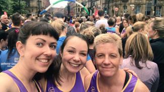 Three women at a running event, huddled together and smiling