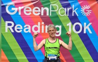 A man in a running vest holding both hands in the air