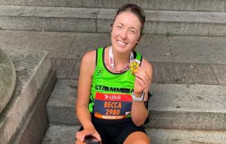 A woman in running gear sitting on a step, holding a medal and smiling