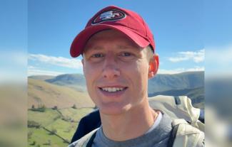 A man in an outdoor setting, wearing a baseball cap and smiling