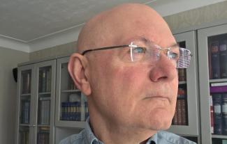 A man in glasses looking to the right, in a contemplative way