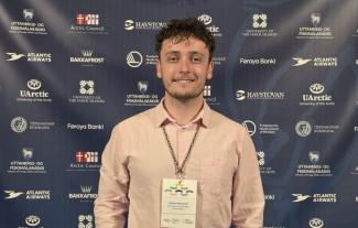 A man in a lanyard smiling, in front of a board covered in logos