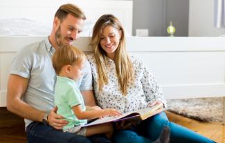 A mother and father sitting with their young son and reading a book