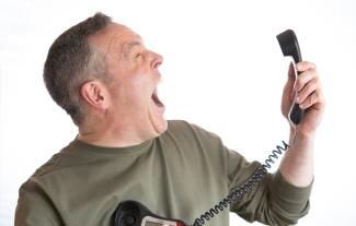 A man holding a telephone receiver in front of him and screaming at it