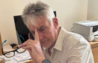 A man looking defeated, with a phone to his ear and his other hand holding a pair of glasses and touching his forehead
