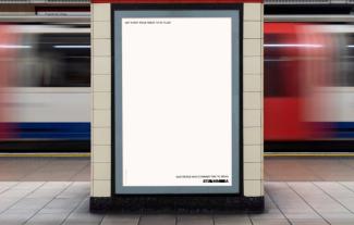 A digital billboard in an underground station, with a tube train speeding past behind it