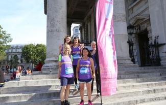 Five women standing on some steps, holding a banner, and dressed in running gear
