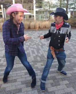 Two men in cowboy outfits pretending to draw fire on each other
