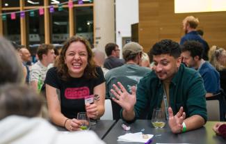 A woman and a man sitting at a table, the woman is laughing and the man is holding his hands out