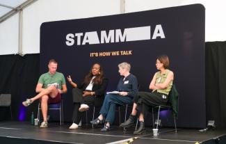 A man and three women sitting on a stage. One of the women is talking and the others are listening