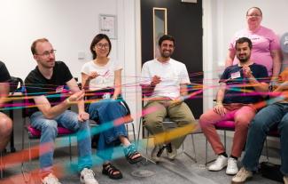 A group of people sitting in a classroom holding a network of different coloured string