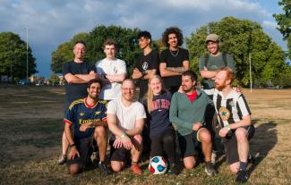 Ten people standing and kneeling together in a park and smiling