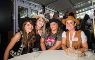 Four women in cowboy hats sitting at a table and smiling
