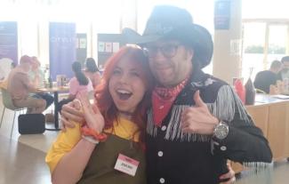 A man in a cowboy outfit posing with a women, both are smiling