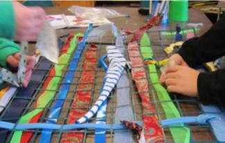 Two pairs of hands creating a mesh-style piece of art, involving strips of fabric and thread
