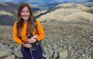 A woman in hiking gear standing on a mountain and smiling