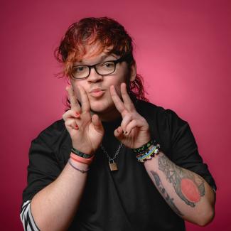 A man wearing glasses, doing two peace signs with his hands and pouting