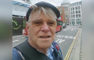 A man with a London street as a backdrop, smiling