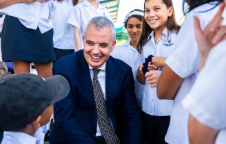 A man in a suit, smiling, surrounded by schoolchildren