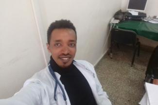 A man in a doctor's uniform, with a stethoscope round his neck, smiling