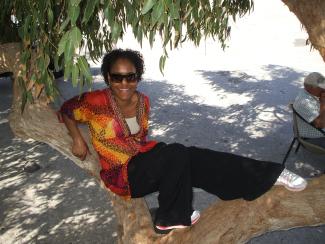A woman in sunglasses sitting on the branch of a tree and smiling