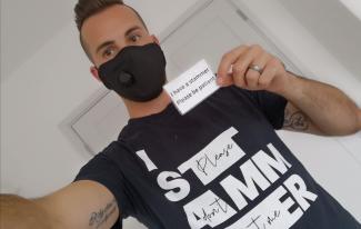 A man in a face mask holding up a card that says 'I have a stammer. Please be patient'