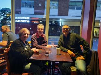 A woman and two men sitting around a cafe table, smiling for the camera