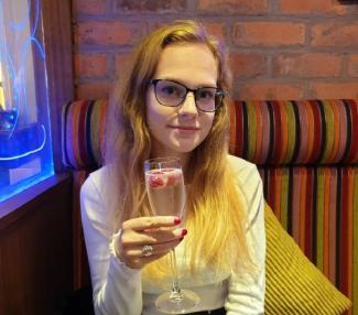 A woman sitting on a chair, holding a glass of champagne up to the camera