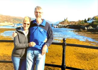 A man standing with his arm around a woman, leaning on a fence in front of a port scene