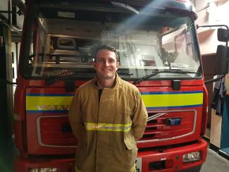 A fireman in uniform standing in front of a fire engine