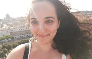 A young woman smiling, with a backdrop of the city of Rome behind her
