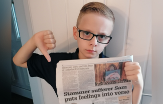 A young boy holding up a newspaper and pointing his thumb down