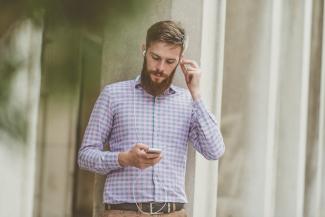 A man looking at a smartphone whilst putting an earphone in one ear