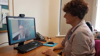A woman sitting at a desk in an office looking at a computer screen while having a video call