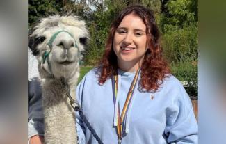 A young woman smiling and standing next to a llama