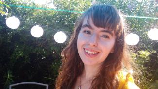 A woman in garden with lights behind her head, smiling for the camera