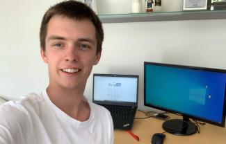 A man smiling in front of two computer screens on a desk