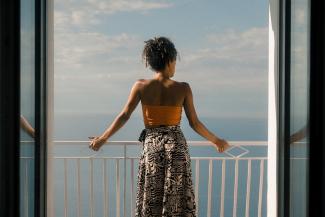 The back of a woman standing on a balcony, looking at the ocean.